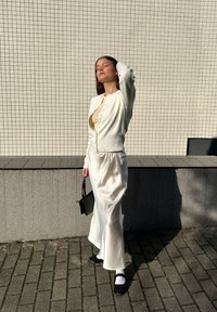 Biały kardigan na beżowej bluzce, w zestawieniu z zwiewną białą satynową spódnicą. Czarna torebka i buty w połączeniu z białymi skarpetkami dopełniają stylizację.
