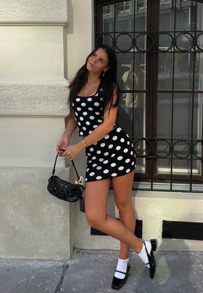 Vestido de lunares en blanco y negro con escote cuadrado, combinado con un pequeño bolso negro y zapatos de charol con calcetines blancos.