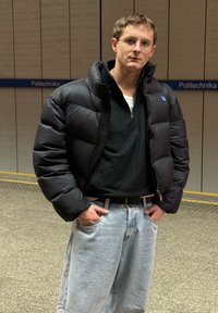 Črna puhovka s prešitim vzorcem, črn zadrgan ovratnik, kombiniran z ohlapnimi svetlo modrimi kavbojkami in črnim pasom. Priložnostni videz.