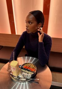 Smoothie korkeassa lasissa pillillä ja pyöreä kulho granolaa, jonka päällä on mansikoita ja mustikoita metallipöydällä.