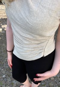 Top justo de tom bege claro com uma superfície texturizada, apresentando franzidos laterais e um fecho de zíper, combinado com leggings curtas pretas.
