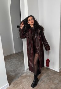 Casaco trench de couro sintético bordô com padrão de pele de cobra, design de duplo abotoamento, combinado com um vestido justo e meias de bolinhas. Botas de plataforma pretas.