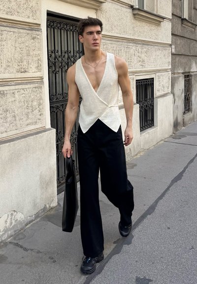Top blanco sin mangas con escote en V profundo, combinado con pantalones amplios negros. Lleva un bolso tote negro y usa zapatillas negras. Textura suave.