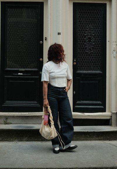 Top blanco de manga corta con detalles de fruncido, jeans de mezclilla de pierna ancha de cintura alta en azul oscuro, bolso beige y zapatos negros.