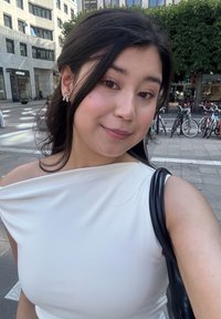 Witte off-the-shoulder top van zachte stof; het onderwerp draagt zilveren vlinder oorbellen. Zwarte handtas op de schouder, stedelijke achtergrond.