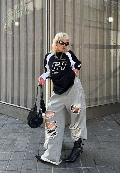 Top de manga larga en blanco y negro con gráfico de "64", pantalones de chándal grises desgastados, botas de tacón negras y un bolso negro. Fondo urbano.
