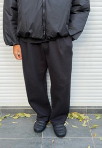 Sort polstret jakke over en mørk t-shirt, kombineret med løse sorte joggingbukser og sorte quiltede slip-on sko. Neutral baggrund med løv.