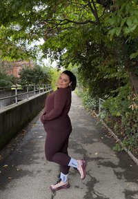Maroon workout set featuring a fitted long-sleeve top and leggings. Accented with light grey sports socks and maroon athletic shoes. Green foliage background.