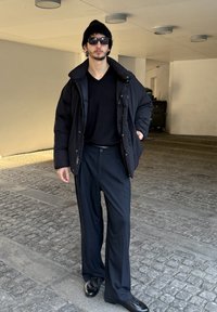 Melna pūderveida jaka pār melnu V-veida apkakles kreklu, kombinēta ar svītrainām biksēm un melniem apaviem. Aksesuāri: saulesbrilles un adīta cepure.