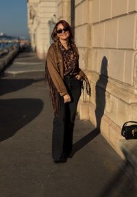 Καφέ σουέτ τζάκετ με κρόσσια πάνω από πουκάμισο με λεοπάρ σχέδιο, μαύρα φουσκωτά τζιν και μαύρα γυαλιά ηλίου. Μικρή μαύρη τσάντα δίπλα.