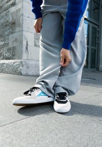 Hvide og sorte sneakers med blå accenter, der har en glat overflade og snørelukning, parret med grå, brede bukser.