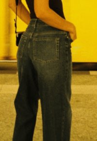 Hochtaillierte blaue Denim-Jeans mit lockerer Passform. Verfügt über zwei Gesäßtaschen und eine glatte Textur. Der Hintergrund ist in einem verschwommenen gelben Farbton.