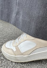 Beżowe i białe sneakersy z teksturowanej skóry i gładkimi akcentami, z okrągłymi sznurowadłami i perforacjami na palcach, na szarym tle.