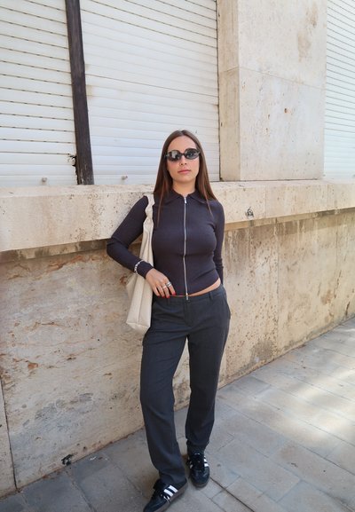 Top oscuro con rayas y cremallera frontal, pantalones grises, zapatillas negras y una bolsa de mano ligera. Presenta un corte recto, estilo ajustado y un diseño minimalista.