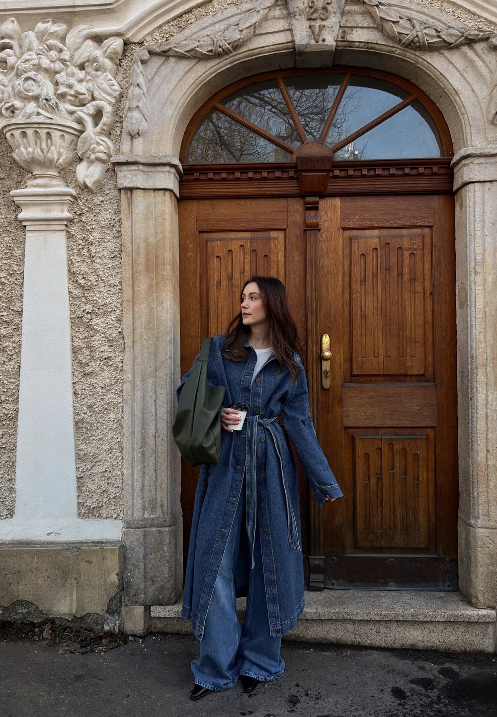 Denim plašč s dolgimi rokavi, ožjim pasom in ohlapnim krojem. Temno denim material v kombinaciji z širokimi hlačami. Olivno zeleno torbo.