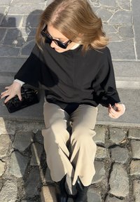 Maglietta nera oversize con scollatura alta, pantaloni beige a gamba larga, stivaletti neri, e una piccola borsa nera con hardware in argento.