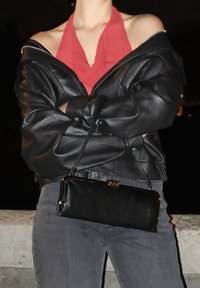 Bolso cruzado de cuero negro con una forma rectangular elegante y herrajes dorados. Combinado con un top halter rojo y una chaqueta de cuero negro.