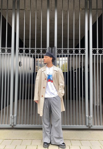 Trench beige con botones grandes, camiseta gráfica blanca con diseño azul y rojo, pantalones de pierna ancha gris y zapatos de plataforma negros.