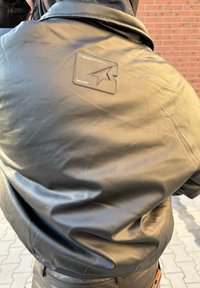 Fekete bőrdzseki sima textúrával, hátul egy csillagmintás téglalap alakú folttal. Az anyag fényesnek tűnik.