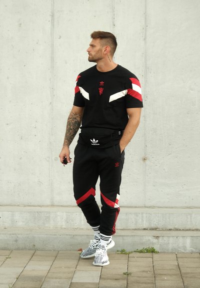 Conjunto atlético negro que incluye una camiseta con acentos y logotipos rojos y blancos, pantalones ajustados con detalles en las franjas y zapatillas con motivo.
