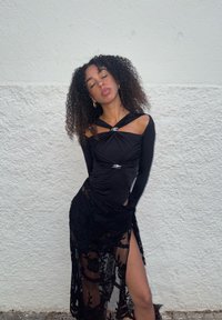 Svart tettsittende topp med lange ermer og vridd design, med sølvdetaljer. Gjennomsiktig svart blonderkjørt med blomsterkanter og sidesplitt.