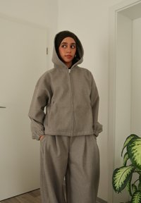 Sweat à capuche gris à fermeture éclair avec capuche et poches kangourou, associé à un pantalon de jogging large assorti. Tissu doux et coupe décontractée.