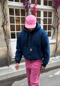 Φούτερ τζιν σε σκούρο μπλε, συνδυασμένο με φωτεινά ροζ παντελόνια φόρμας. Ένα ανοιχτό ροζ καπέλο ολοκληρώνει την εμφάνιση. Λουλουδάκια κοσμούν το φόντο.