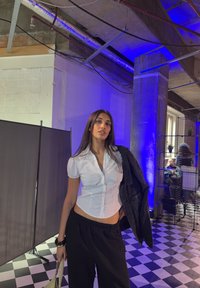 Weißes Hemd mit Knöpfen, schwarze lockere Hose und dunkle Jacke. Die Umgebung hat einen schachbrettartigen Boden und blaues Ambientelicht.
