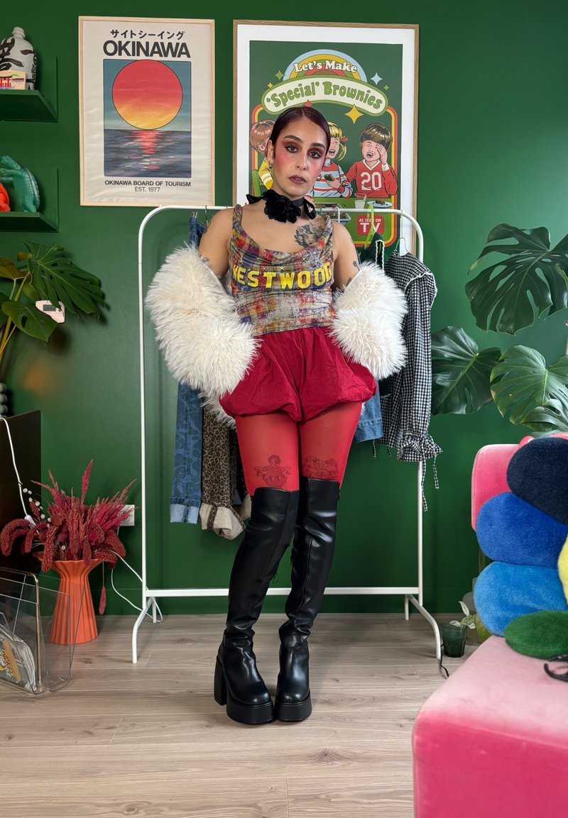 Färgstarkt outfit med en mångfärgad Westwood-linne, röda puffiga shorts, genomskinliga röda strumpbyxor med mönster och knähöga svarta stövlar.