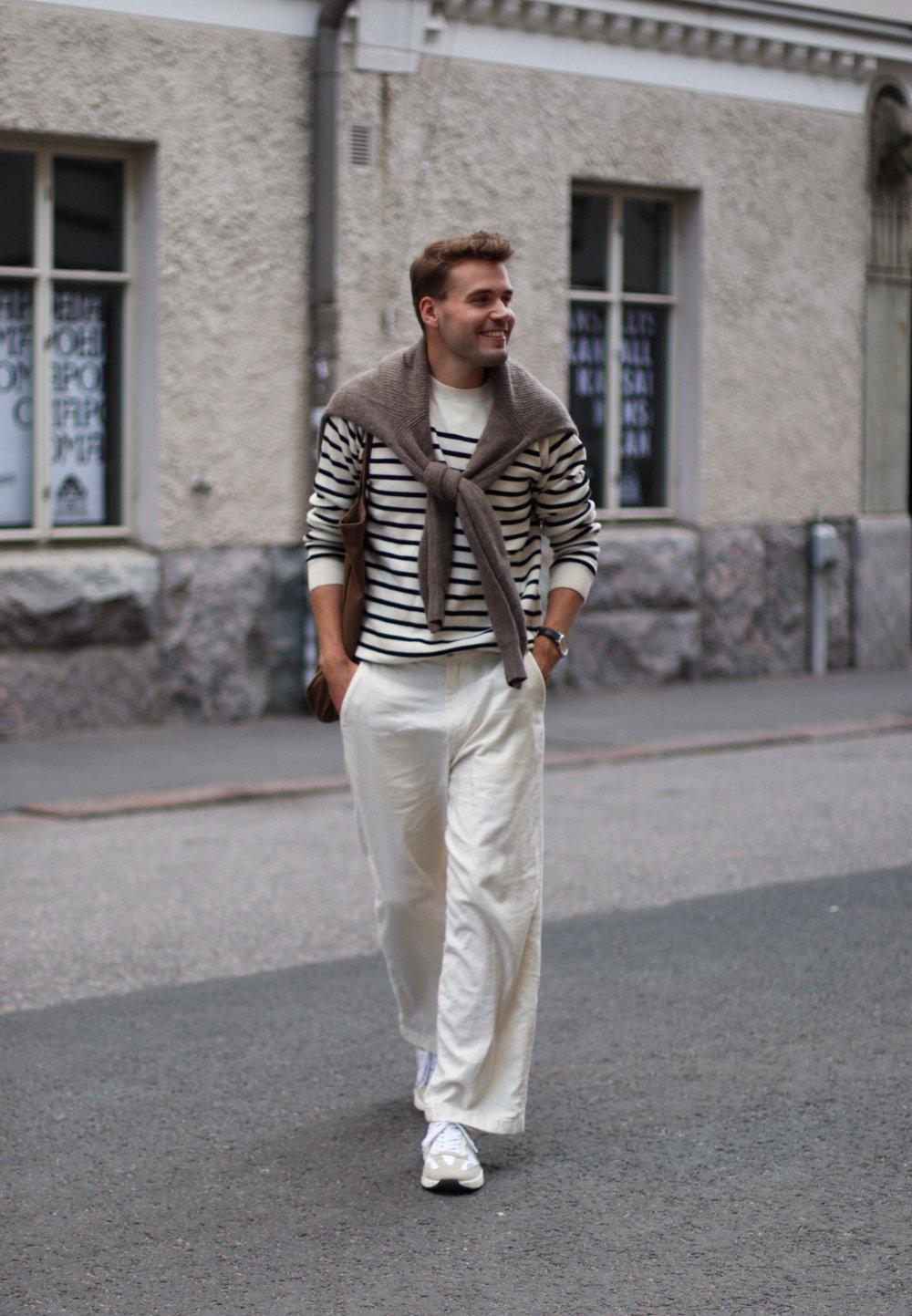 Striped jumper in white and navy, beige scarf draped around the neck, white trousers, and white trainers, carrying a brown bag.