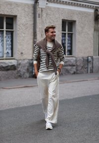 Striped jumper in white and navy, beige scarf draped around the neck, white trousers, and white trainers, carrying a brown bag.