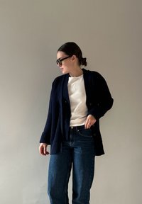 Mornaric ribanasti kardigan z gumbom, oblečen čez svetlo pulover. Ujemajo se z modrimi jeans hlačami z visokim pasom, ki imajo sproščen kroj.