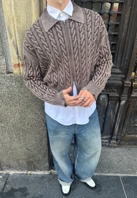 Casaco de malha com fecho de correr em castanho claro e modelo de ponto torcido, usado sobre uma camisa branca de botões. Combina com jeans de lavagem clara e corte largo e mocassins pretos.