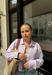 Gestreepte roze overhemd, denim shorts, geweven rieten tas met leren accenten, gelaagde sieraden en een bloem in de tas gestoken.