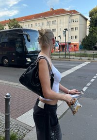 Bolso de cuero negro con cadena, camiseta blanca ajustada, jeans negros de cintura alta con bolsillos, sosteniendo una bolsa de palomitas.