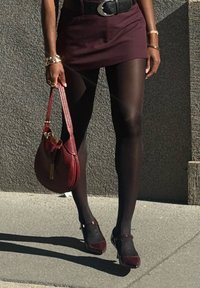 Bordeaux mini seelik, mis on ühendatud läbipaistvate mustade sukkpükstega, burgundi värvi käekott ja sobivad suletud nina tallad koos pahkluu rihmaga. Esitatud on tekstureeritud materjalid.