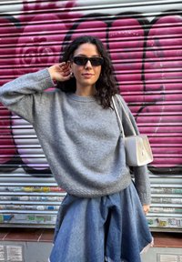 Grey wool jumper with dropped shoulders, paired with a denim skirt. Accessories include black sunglasses and a small white handbag.