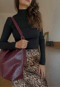 Schwarzes langärmliges Rollkragenoberteil kombiniert mit einem Rock im Leopardenmuster. Zubehör umfasst eine bordeauxfarbene, strukturierte Tasche und einen silbernen Kettengürtel.