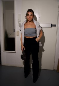 Sivi top bez naramenica, svijetlosiva pamučna majica prebačena preko ramena, crne hlače visokog struka, mala torbica, s običnim bijelim vratima u pozadini.