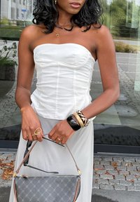 Biały top bez ramiączek z wyraźnym przeszyciem, szara zwiewna spódnica, torebka z wzorem oraz wiele bransoletek na nadgarstku.