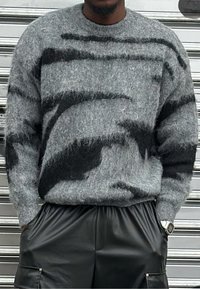 Suéter gris de punto con textura peluda y patrones abstractos negros, cuello redondo y puños acanalados, combinado con shorts de cuero negros.