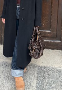 Manteau noir, jean denim foncé retourné, bottines marron clair et sac en cuir marron avec une surface texturée et des détails en métal doré.