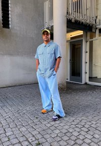 Svetlo modri široki hlače, denim srajca s kratkimi rokavi, rumena kapica, večbarvni čevlji, stojijo ob betonski steni.
