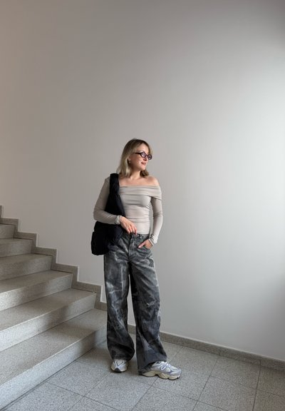 Top de manga larga gris claro sin hombros, pantalones anchos grises con patrón y zapatillas grises, con un bolso negro colgado de un hombro.