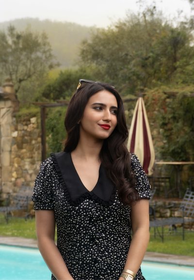 Vestido negro con lunares blancos, mangas cortas abullonadas y un cuello negro con volantes. Llevado con un accesorio para el cabello dorado y una pulsera.