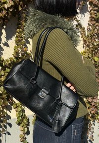 Schwarze Lederhandtasche mit strukturierter Oberfläche, rechteckiger Form, silberner Hardware und zwei Griffen, vor einem grünen Hintergrund präsentiert.