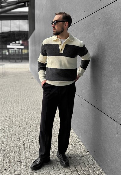 El suéter presenta franjas horizontales en negro y crema, tejido texturizado y un cuello tipo polo. Se combina con pantalones negros y mocasines negros.