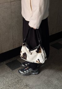 Λευκή και καφέ δερμάτινη τσάντα με υφή, κοντές μαύρες λαβές και φερμουάρ στην κορυφή. Φοριέται με μια μακριά μαύρη φούστα και αθλ�ητικά παπούτσια.