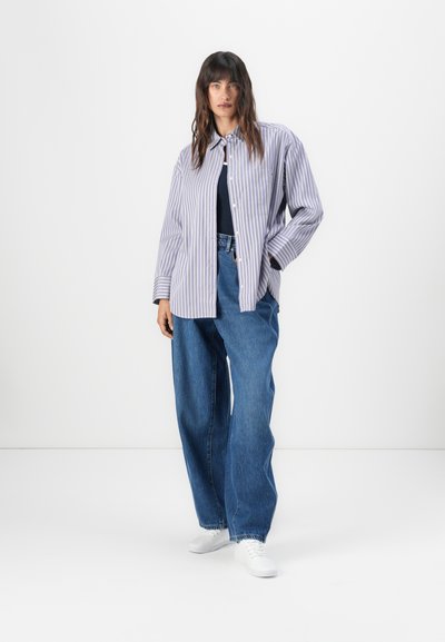 Camisa de botones a rayas en púrpura claro y blanco, combinada con jeans de mezclilla azul holgados y zapatillas blancas. Diseño sencillo y relajado.