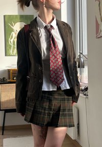 Brun kordfløyelsblazer over en hvit skjorte, rød mønstret slips og et rutete skjørt. Antrekket har tydelige teksturer og farger.